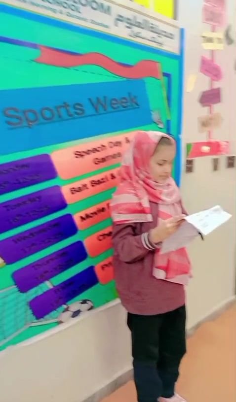Student giving a speech in front of the Sports Week board